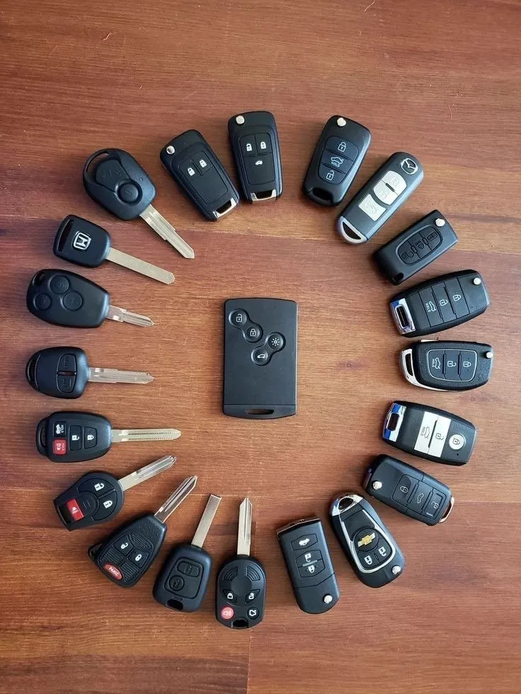 Colección de llaves y mandos de carro dispuestos en círculo sobre una mesa de madera.